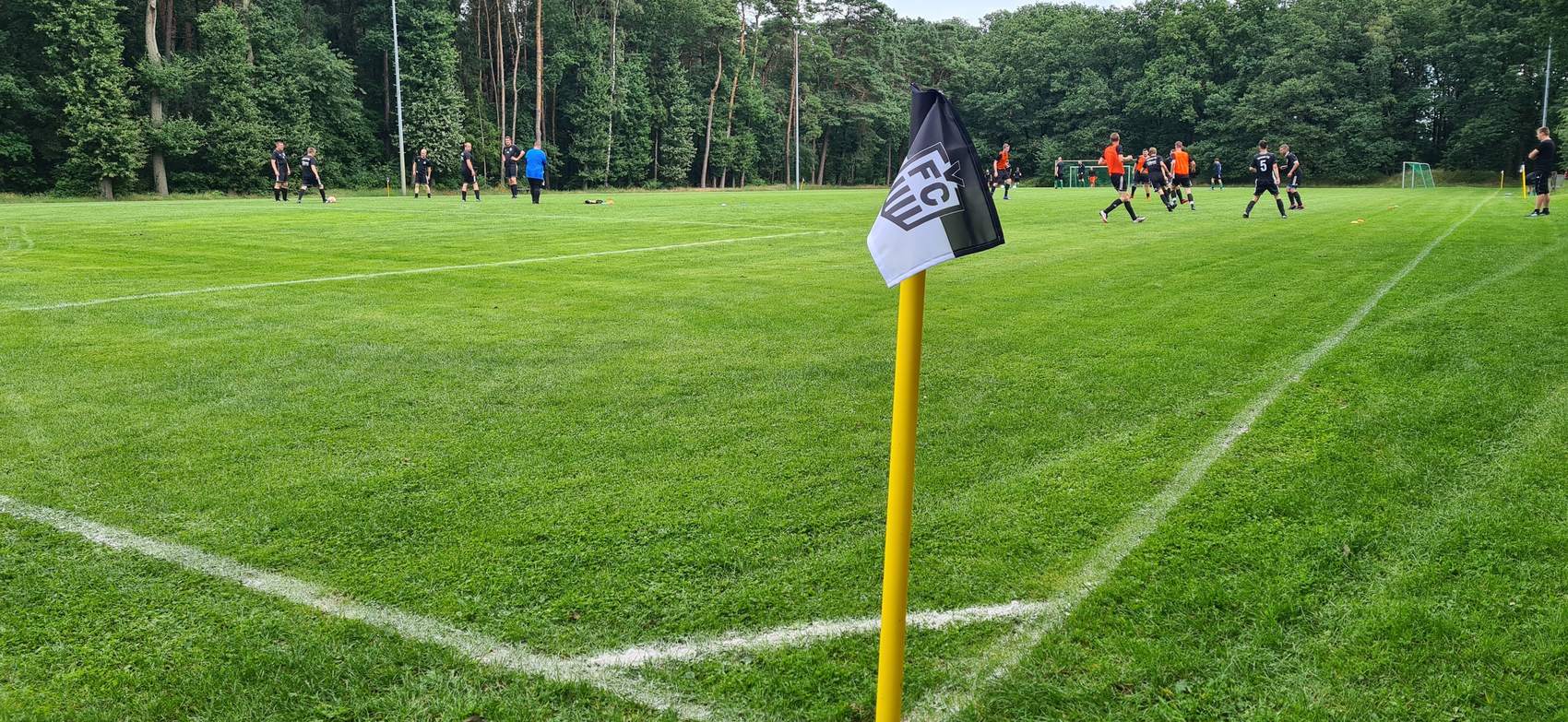 Eckfahne mit dem Wappen des Veeser FC, dahinter läuft ein Spiel auf dem Sportplatz