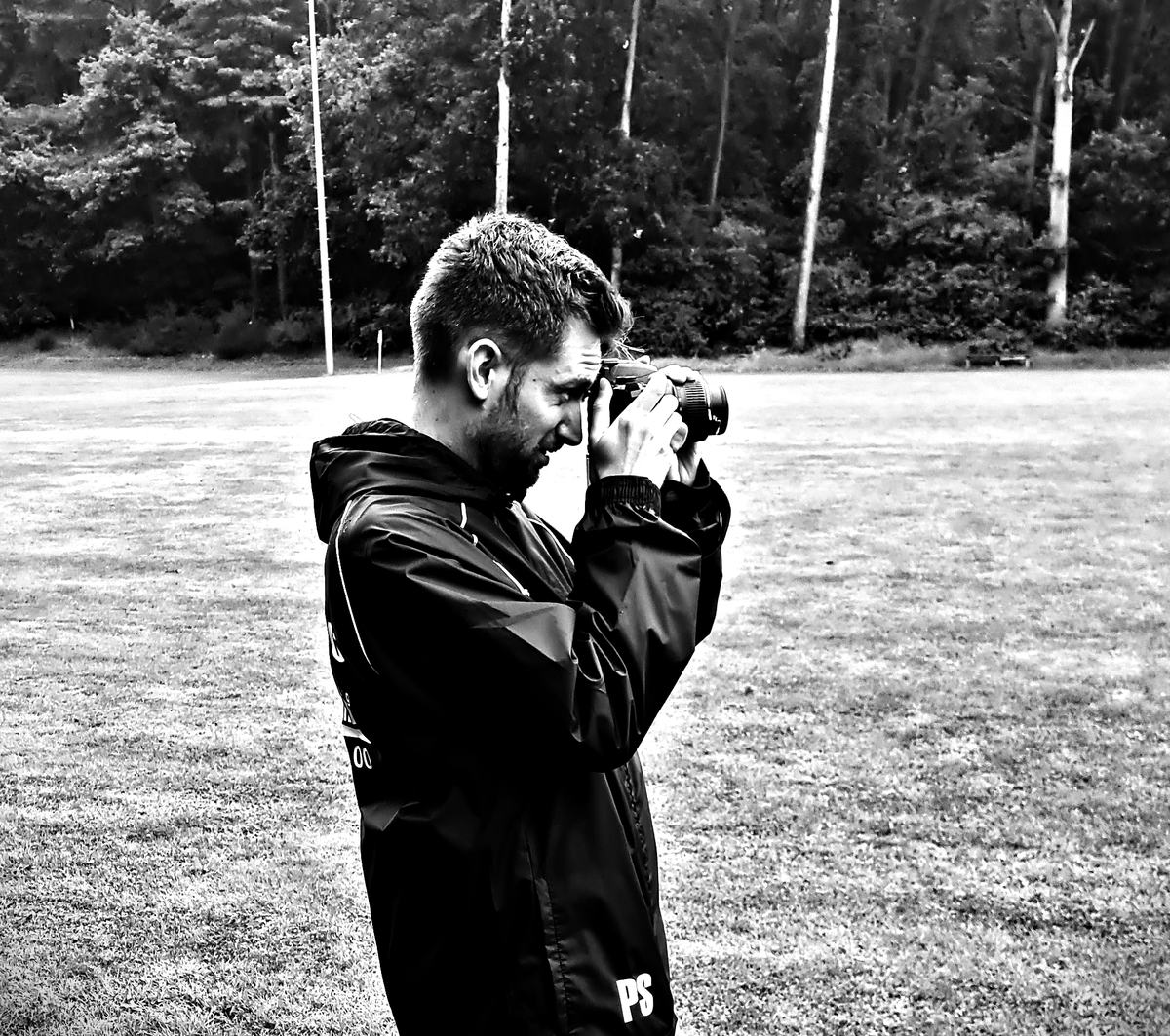 Ein Vereinsmitglied fotografiert in Vereinsjacke am Spielfeldrand